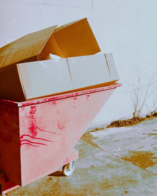 A person’s arm extending into the frame from the left holds a tied green plastic trash bag, which appears to contain waste and has a slightly dented surface. The bag's top is gathered and knotted, w