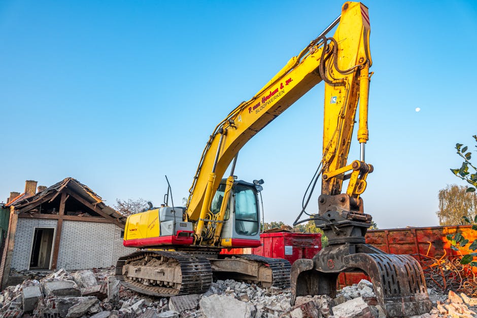 A yellow Hyundai hydraulic excavator with a long arm and bucket attachment is operational amidst a large pile of rubble, including broken concrete, twisted metal, black plastic sheeting, and discarded